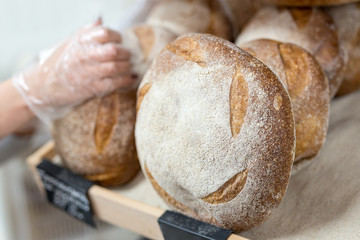 Baker's hand putting Loafs of warm tasty freshly baked bread in a bakery shop or market