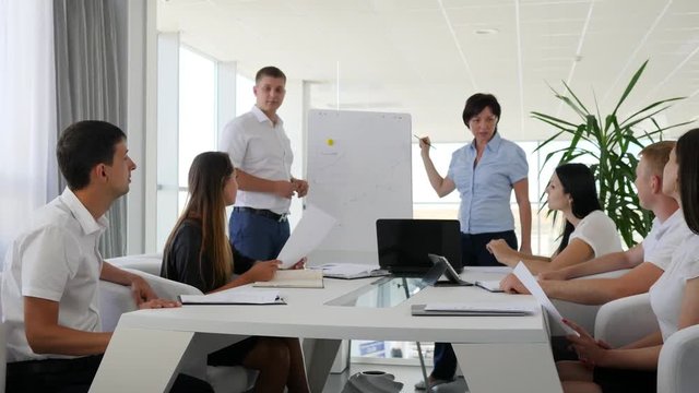 colleagues giving presentation near flipchart for partners at meeting in white and spacious office