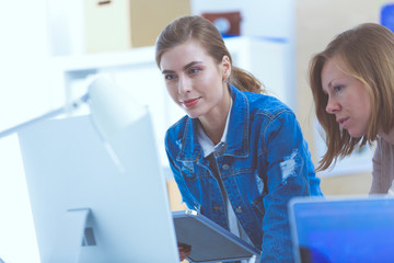 Two young woman standing near desk with instruments, plan and laptop.