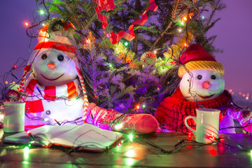 Family of snowmen celebrates Christmas at festive table with tea and book. Plans for next year, total for the year. Snowmen as married love couple celebrate new year. Christmas tree and Christmas mood