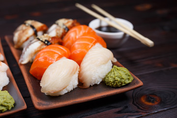 Delicious appetizing nigiri sushi, served on clay plates with soy sauce and chopsticks on dark...