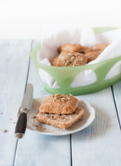 Homemade square breakfast bread rolls made from whole grain flour, sunflour seeds, sesame seeds and various other seeds and grains in bread basket standing at light blue wooden table with vintage b