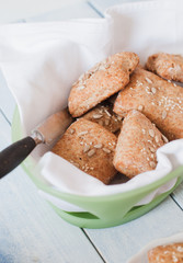 Homemade square breakfast bread rolls made from whole grain flour, sunflour seeds, sesame seeds and various other seeds and grains in bread basket standing at light blue wooden table with vintage b