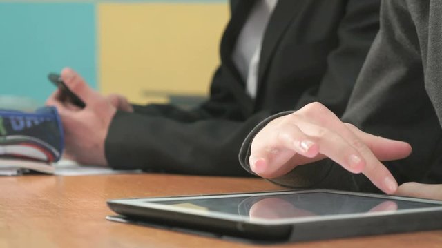 Two students sit at desk at office. One man holding smartphones other man looking at white-black computer tablet pressing them fingers on screen and look at important information