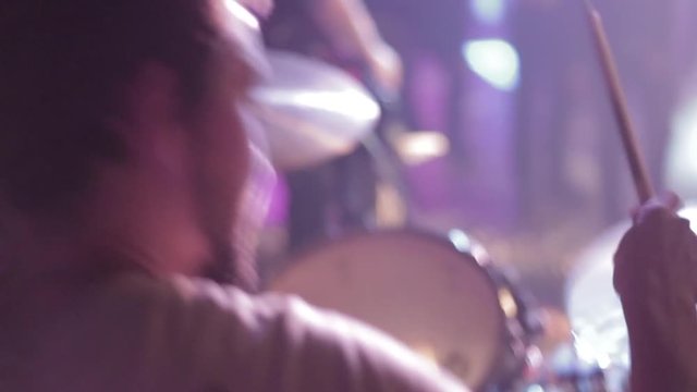 close-up from back the drummer with view at musicians rock band and fans in blur