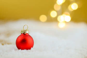 Red Christmas ball in a snow on golden background.