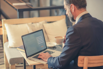 Senior mature business man having a coffee in a coffee shop and working on his laptop