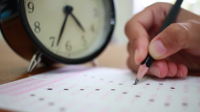 Students taking exams writing on optical form of standardized exam near Alarm clock with holding yellow pen for final examination in secondary school, college university classroom, Education concept