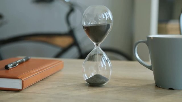 Close up shot of sand falls quickly in the hourglass in the office background.