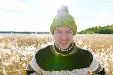 Young happy handsome man smiling against scenic view of autumn bullrush field