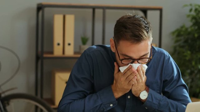 Portrait of sick and tired businessman sneezing while working in the office. Close up