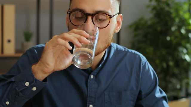 Portrait of tired, sick businessman in the stylish glasses taking pill during work time in the modern office. Taking medecine. Close up