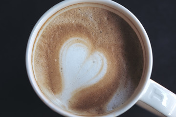 Close up image of hot coffee with heart latte art in white mug and black background