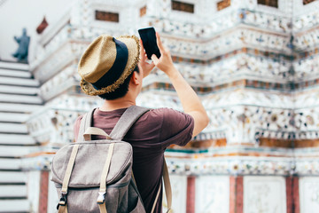 Young Asian traveling backpacker taking photos with smartphone in Wat Arun in Bangkok, Thailand