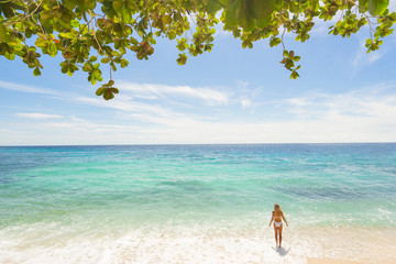 Fototapeta na wymiar Girl in white swimwear standing on the beach. Blue sky and green leaves on background.