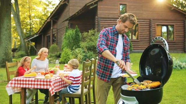 Happy nice family having barbeque near their wooden house in the green garden. Sunny weather. Outdoors