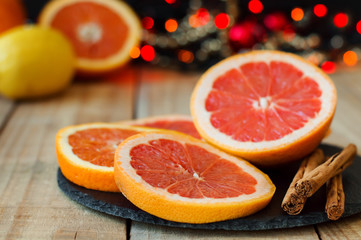 Fototapeta na wymiar Horizontal photo of fresh grapefruit and orange with cinnamon sticks served on black slate board on wooden table with christmas lights. Christmas atmosphere