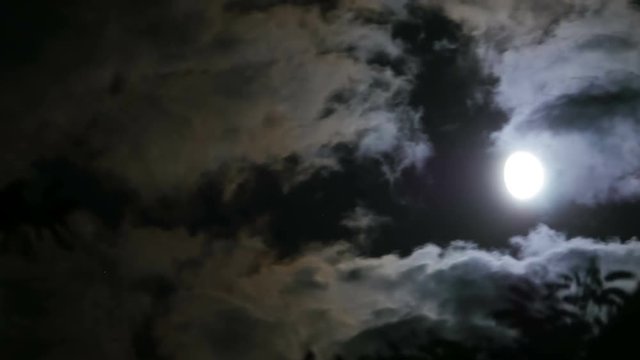 Full Moon Moves through the Clouds in the Night Sky through which it Shines. Timelapse. Dark clouds moving through the full moon on a black sky. Moon light.