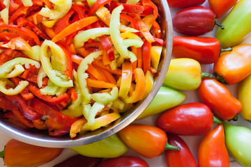 Part of round metal bowl wiht pieces of multi-colored peppers and whole uncut peppers.