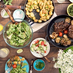 Dinner table with grilled steak, vegetables, potatoes, salad, snacks, lemonade