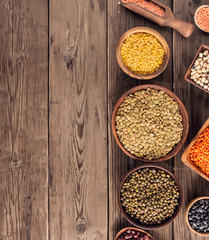 Set of various beans and colorful lentils in bowls and box on wooden background, top view with copy space