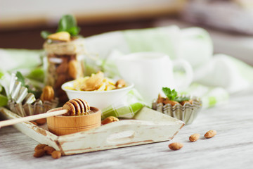 Honey in the bowl, muesli, mint leaves, almonds and jar with milk on the wooden tray