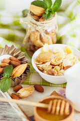 Honey in the bowl, muesli, mint leaves, almonds and jar with milk on the wooden tray