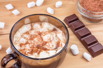 Glass cup of coffee with marshmallows and chocolate on wooden background