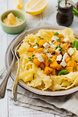 Pasta Mafaldine Napoletane with baked pumpkin, feta cheese and seasoning herbs in ceramic plate on white wooden background. Selective focus. Rustic style. Top view.