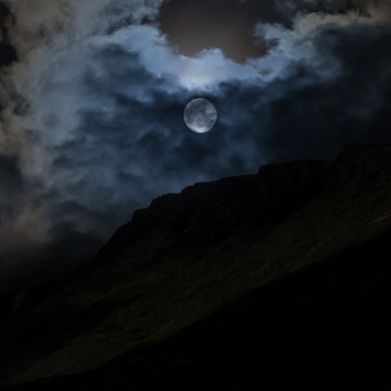The moon behind the clouds in the night sky over the top of the mountain.