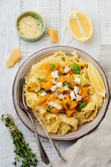 Pasta Mafaldine Napoletane with baked pumpkin, feta cheese and seasoning herbs in ceramic plate on white wooden background. Selective focus. Rustic style. Top view.