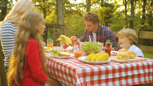 Happy family having a good time while sitting at the table in the green beautiful backyard on a sunny summer day. Outside