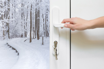 Naklejka premium Welcome winter. Woman's hand at home opening the white plastic door with view on snow covered trail and trees. Winter day concept.