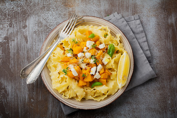 Pasta Mafaldine Napoletane with baked pumpkin, feta cheese and seasoning herbs in ceramic plate on gray concrete old background. Selective focus. Rustic style. Top view.