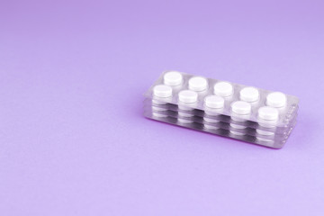 Packs of white pills packed in blisters with copy space on purple background. Focus on foreground, soft bokeh