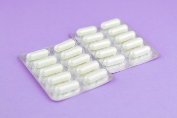 Packs of white capsules packed in blisters with copy space on purple background. Focus on foreground, soft bokeh