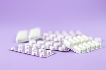 Packs of white capsules and pills packed in blisters with copy space on purple background. Focus on foreground, soft bokeh