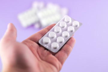The man hand is holding a pack of white pills packed in blisters with copy space on purple background. Focus on foreground, soft bokeh