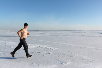 Man in a cap with a naked torso running across the ice of a frozen river, Ob Reservoir, Russia
