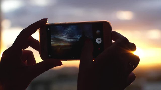 Women hands taking photo of sunset city view with her mobile phone in slow motion and lense flare effects. 3840x2160, 4k