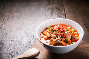 Red curry with pork and coconut milk, delicious Thai food on wooden table.