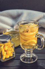 Tea with ginger and lemon in a glass cup and yellow sweets on a wooden background