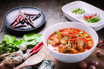 Red curry with pork and coconut milk, delicious Thai food on wooden table.