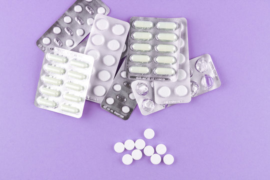 Full and empty packs of white capsules and pills packed in blisters with copy space on purple background. Focus on foreground, soft bokeh
