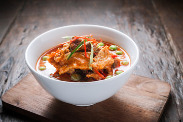 Red curry with pork and coconut milk, delicious Thai food on wooden table.