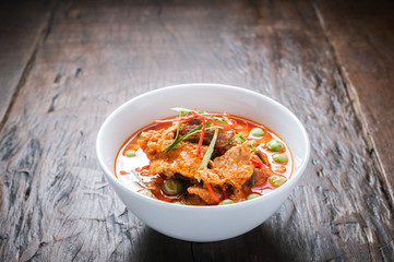 Red curry with pork and coconut milk, delicious Thai food on wooden table.