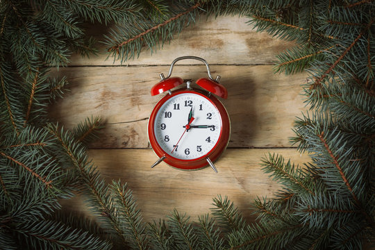 An image of an alarm clock on a wooden table with Christmas tree branches