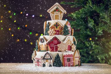 Large tiered Christmas cake decorated with gingerbread cookies and a house on top. Tree and...
