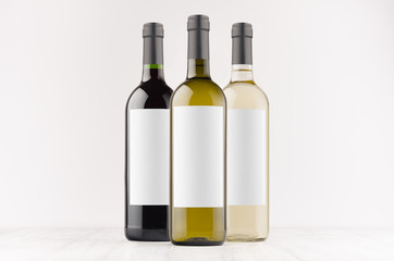 Set wine bottles - transparent, green, black- with blank white labels on white wooden board, mock...