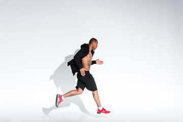 side view of young african american man in sportswear running on grey